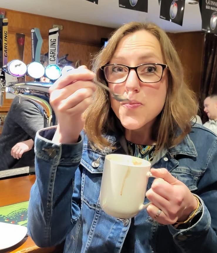 Jenny, founder of The Teabreak Project, holding a mug and spoon in a café